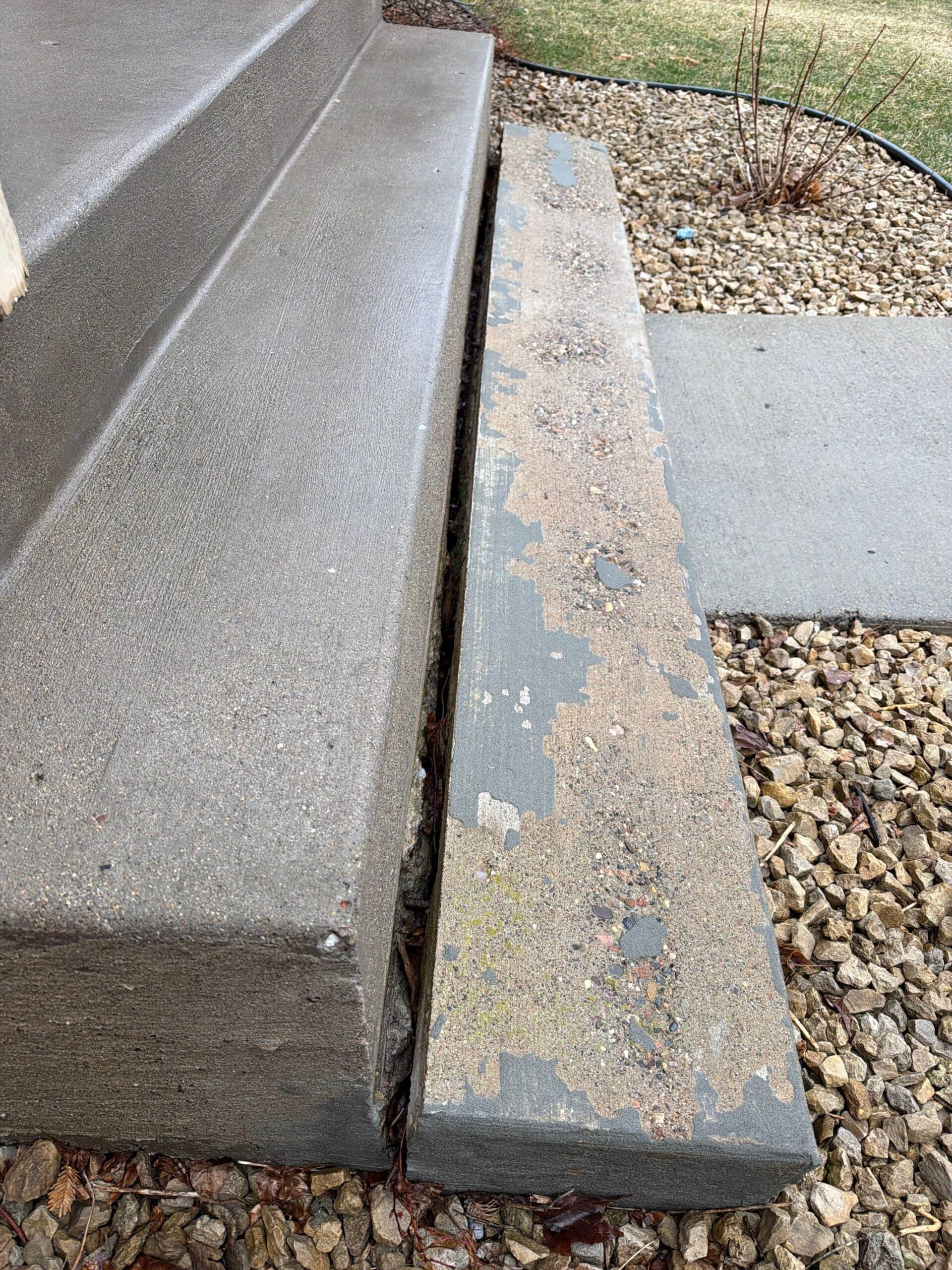 A concrete porch step with peeling and worn surface next to gravel landscaping and a concrete walkway. The step shows exposed aggregate and patches of missing top layer.